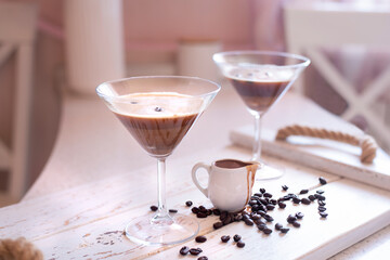 Espresso Martini cocktail in a martini glass decorated with coffee beans and a small jug with coffee liqueur in a bright interior