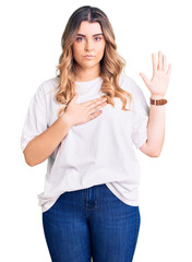Young caucasian woman wearing casual clothes swearing with hand on chest and open palm, making a...