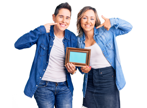 Couple of women holding empty frame smiling cheerful showing and pointing with fingers teeth and mouth. dental health concept.