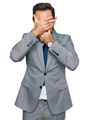 Middle age man wearing business clothes covering eyes and mouth with hands, surprised and shocked. hiding emotion