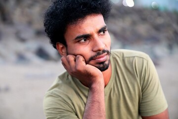 Thoughtful young man with a beard resting his chin on his hand looking away with a blurred background