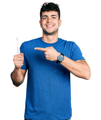 Young hispanic man holding electric toothbrush smiling happy pointing with hand and finger