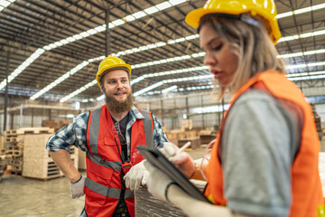 Team workers carpenter wearing safety uniform and hard hat working and checking the quality of wooden products at workshop manufacturing. man and woman workers wood in dark warehouse industry.