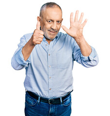 Senior man with grey hair and beard wearing casual blue shirt showing and pointing up with fingers...