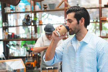 Smart Caucasian male enjoy drinking a takeaway hot coffee in front of coffee shop or café bar or counter, Refreshment, happiness good taste and aroma from coffee. Man is holding hot americano or latte
