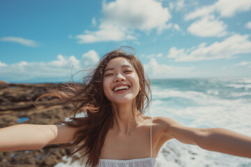 Happy asian woman with open arms and closed eyes on a rocky beach. Concept of freedom