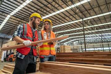 Team workers carpenter wearing safety uniform and hard hat working and checking the quality of wooden products at workshop manufacturing. man and woman workers wood in dark warehouse industry.