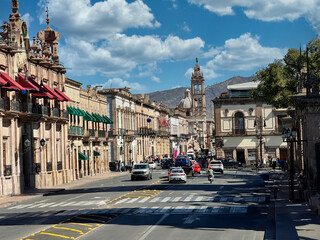 Dynamic street view of Madero Street in Morelia, featuring historic colonial architecture and daily urban life against a mountain backdrop.
