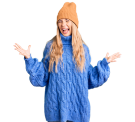 Beautiful caucasian woman with blonde hair wearing wool sweater and winter hat crazy and mad shouting and yelling with aggressive expression and arms raised. frustration concept.