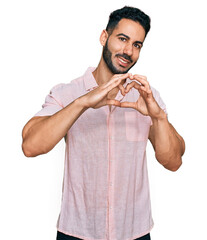 Hispanic man with beard wearing casual shirt smiling in love doing heart symbol shape with hands. romantic concept.