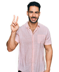 Fototapeta premium Hispanic man with beard wearing casual shirt showing and pointing up with fingers number two while smiling confident and happy.