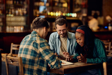 Multiracial group of happy friends looking at menu in pub.
