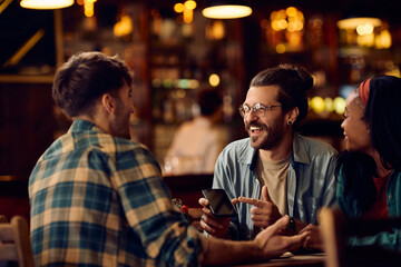 Young man showing something funny on cell phone to his friends in bar.