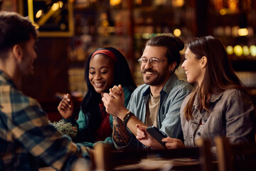 Multiracial group of happy friends talking in pub. - obrazy, fototapety, plakaty