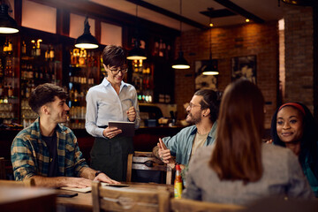 Happy waitress taking order from customers in pub.