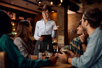 Happy waitress talking to group of guests in bar.
