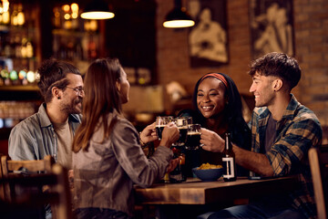 Multiracial group of happy friends toasting with beer while gathering in pub.