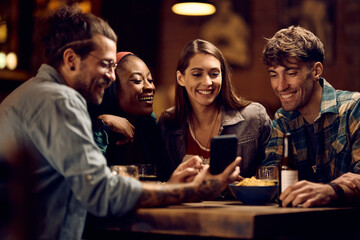 Group of happy friends using smart phone in pub. - obrazy, fototapety, plakaty