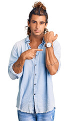 Young hispanic man wearing summer style in hurry pointing to watch time, impatience, looking at the...