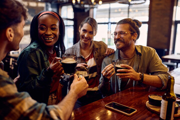 Happy black woman and her friends toasting with beer in bar.