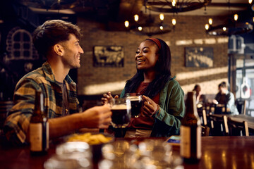 Happy black woman and her boyfriend talk while drinking beer in bar.