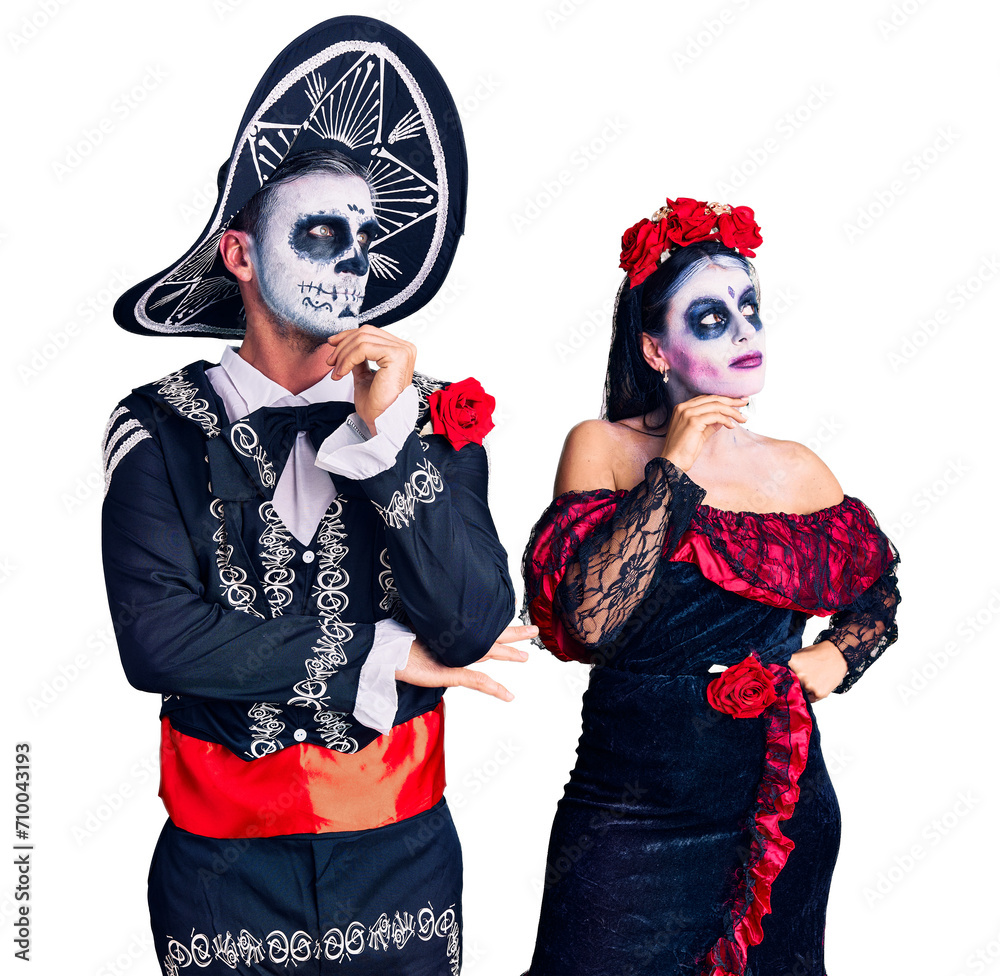 Wall mural young couple wearing mexican day of the dead costume over background with hand on chin thinking abou