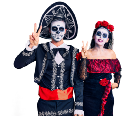 Young couple wearing mexican day of the dead costume over background smiling looking to the camera showing fingers doing victory sign. number two.