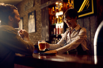 Happy female barista serving beer to guest at bar counter.