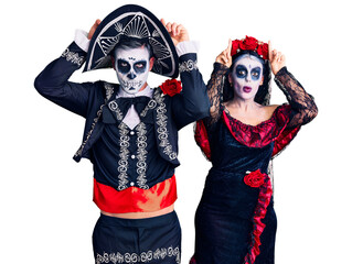 Young couple wearing mexican day of the dead costume over background doing funny gesture with finger over head as bull horns