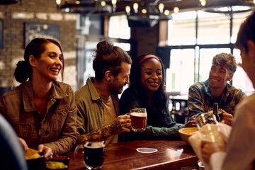 Multiracial group of happy friends drinking beer at bar counter.