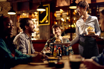 Happy waitress serving food to group of guests in pub.