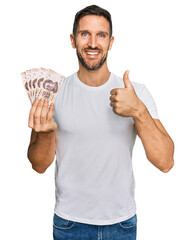 Handsome man with beard holding 50 mexican pesos banknotes smiling happy and positive, thumb up doing excellent and approval sign