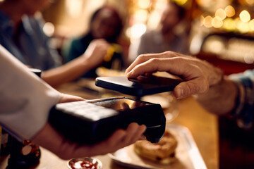 Close up of man paying with cell phone while being with friends in bar.