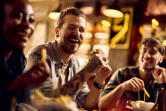 Young man laughing and having fun while eating with his friends in pub.