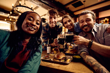 Multiracial group of happy friends taking selfie while gathering in bar.