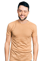 Fototapeta premium Hispanic man with beard wearing casual t shirt winking looking at the camera with sexy expression, cheerful and happy face.