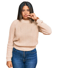 Young latin girl wearing wool winter sweater mouth and lips shut as zip with fingers. secret and...