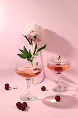 Modern still life with pink martini, alcoholic cocktail, cherry berries and peony flowers on...