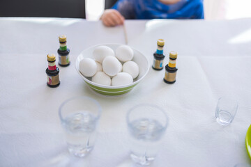 Close-up view of a table covered with paper, featuring a cup of boiled eggs and bottles of food coloring prepared for Easter egg coloring with a child. Sweden.