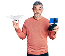 Middle age hispanic man with grey hair using drone with remote control puffing cheeks with funny face. mouth inflated with air, catching air.