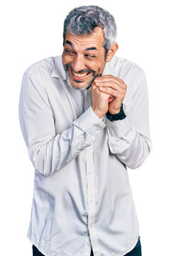 Middle age hispanic with grey hair wearing casual white shirt laughing nervous and excited with hands on chin looking to the side