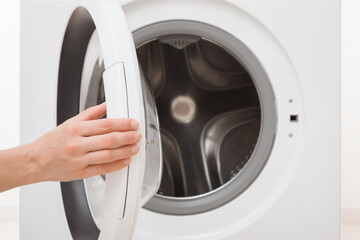 Young adult woman hand opening or closing door of white washing machine. Closeup. Front view. Empty metal drum.
