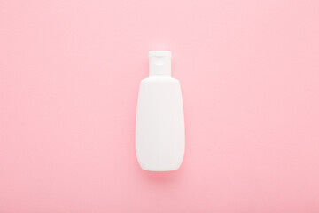 White plastic cream bottle on light pink table background. Pastel color. Care about face, hands, legs and body skin. Closeup. Top down view. Empty place for text or logo.