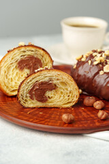 Chocolate croissant on clay plate with cup of coffee on table