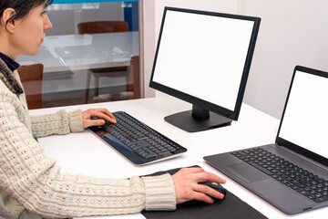 A woman working in the office driving a desktop computer and a laptop. Copy space on screen