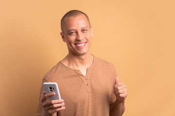 happy brazilian man smiling and holding mobile phone in all beige colors. app, social media,...