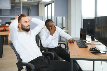 Two diverse colleagues traders talking to each other, sitting in the office in front of multiple computer screens. Stock trading, people, business concept