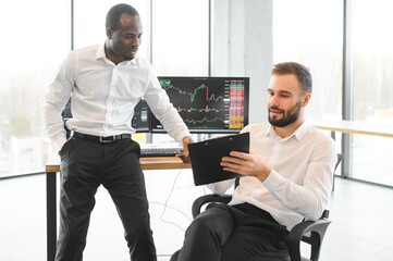 Two confident businessmen, financial analysts or investment advisers sitting at office desk