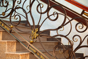 Staircase and railings with forged decor. Steps and metal pattern with bronze and gold patina.