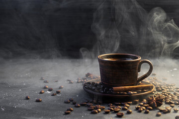A cup of hot fragrant coffee on a dark table. Roasted coffee beans and cinnamon sticks. Steam from a hot drink